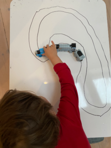 Ein Kind spielt mit einer Spielzeugeisenbahn an einem Whiteboard, das auf dem Tisch liegt und auf das eine Eisenbahnstrecke gemalt wurde.
